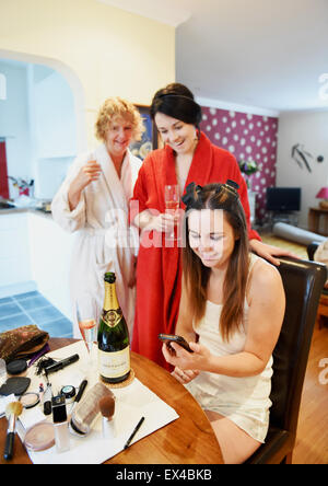 Junge Braut sitzen umgeben von Familie, wie sie für den großen Tag Champagner trinken bereitet Stockfoto