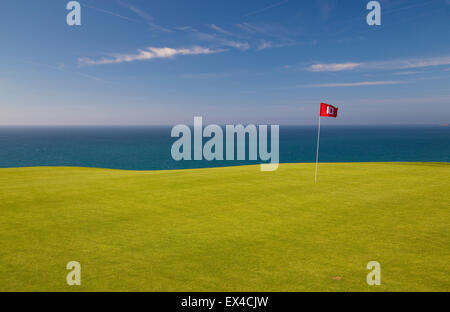 Roter Golf Fähnchen auf grün mit blauem Meer und Himmel dahinter. Stockfoto