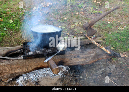 Marschierenden Topf wird über die Kamine auf den Kohlen stehen in der Startaufstellung zum Grillen auf zwei Protokolle geheizt, und eine Axt stecken Stockfoto