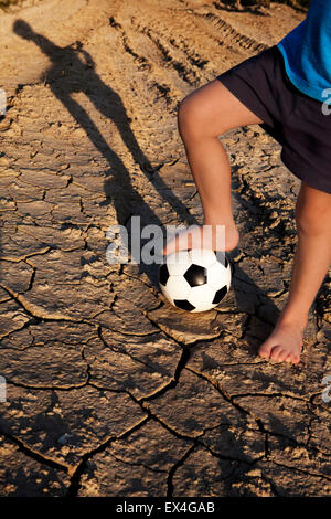 Lass uns Fußball spielen! Junge mit Ball auf Dorfstraße auf trockenem Boden. Stockfoto