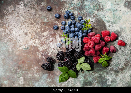 Verschiedene frische Beeren mit Blättern auf Metall Hintergrund Stockfoto