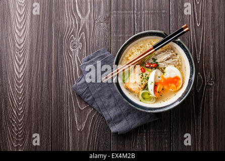 Chinesische Nudeln mit Ei, Tofu und Enoki in Schüssel auf grauem Hintergrund aus Holz Stockfoto