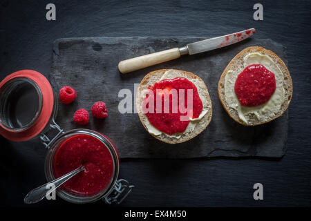 Öffnen Sie Glas von rohen Himbeere & Chia Marmelade und Brot Brötchen mit Butter und Marmelade auf Schiefer Tafel. Ansicht von oben Stockfoto