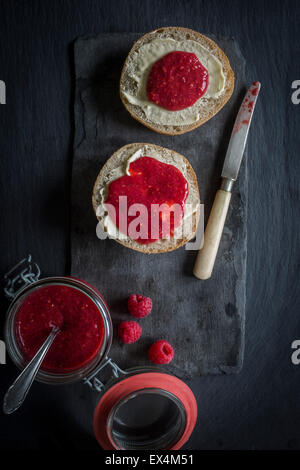 Öffnen Sie Glas von rohen Himbeere & Chia Marmelade und Brot Brötchen mit Butter und Marmelade auf Schiefer Tafel. Ansicht von oben Stockfoto