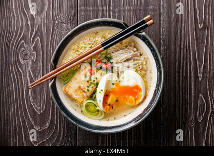 Asiatische Miso Ramen-Nudeln mit Ei, Tofu und Enoki in Schüssel auf grauem Hintergrund aus Holz Stockfoto