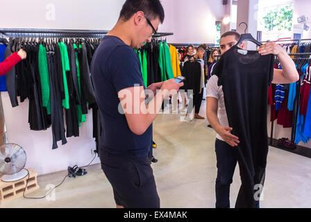 Paris, Frankreich, asiatischen Mann (Modell freigegeben) mit Iphone zum Einkaufen im Marais-Viertel. "Sandro", Marken Fashion Bekleidungsgeschäft, Kaufmann/-Frau zeigt Frau Kleid Stockfoto