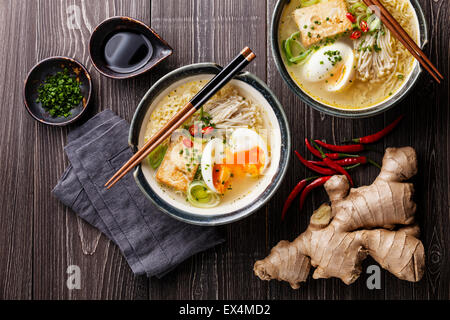 Asiatische Miso Ramen-Nudeln mit Ei, Tofu und Enoki in Schalen auf grauem Hintergrund aus Holz Stockfoto