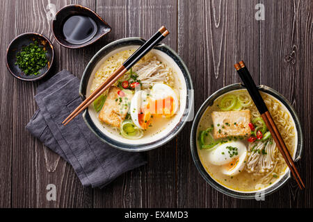 Asiatische Miso Ramen-Nudeln mit Ei, Tofu und Enoki in Schalen auf grauem Hintergrund aus Holz Stockfoto