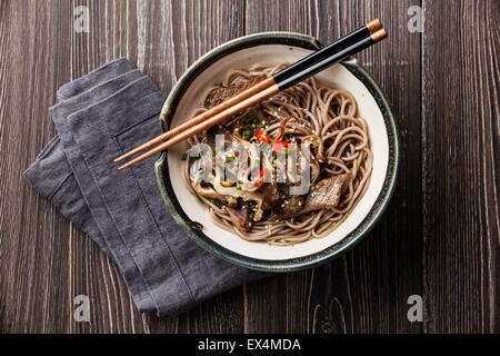 Asiatische Nudeln mit Rindfleisch und Austernpilzen in Schüssel auf grauem Holz Hintergrund Yakisoba Stockfoto