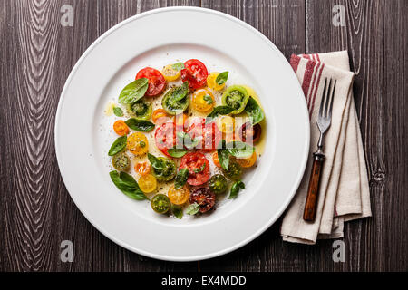 Reife frische bunte Tomaten-Salat mit Basilikum und Olivenöl auf grauem Hintergrund aus Holz Stockfoto