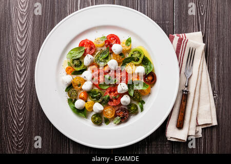 Reife frische bunte Tomaten-Salat mit Basilikum und Mozzarella Mini auf grauem Hintergrund aus Holz Stockfoto