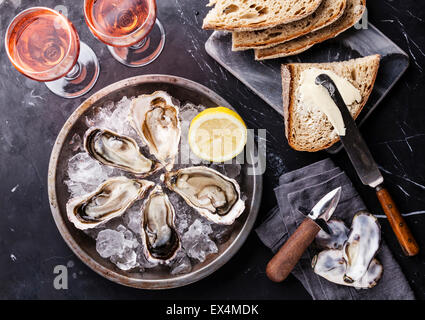 Austern auf Metallplatte mit dunklem Brot mit Butter und Rosé auf dunklem Marmor eröffnet Stockfoto