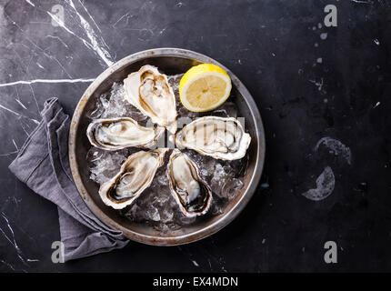 Austern auf Metallplatte mit Eis und Zitrone auf dunklem Marmor eröffnet Stockfoto