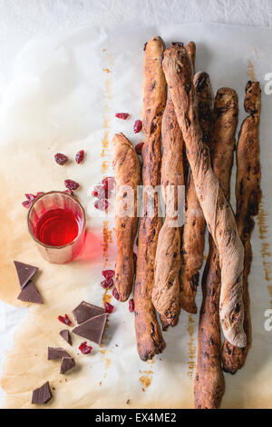 Frisch gebackene hausgemachte süße Schokolade Grissini Brot Sticks über Backpapier mit Glas roten Beeren Likör auf weiße Tischdecke Stockfoto