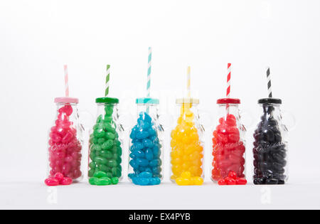 Glasflaschen gefüllt mit verschiedenen bunten Geleebohnen mit passendem Deckel und Strohhalme, vor einem weißen Hintergrund gesetzt. Stockfoto