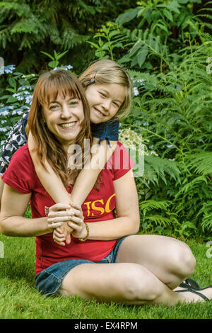 Siebenjähriges Mädchen umarmt ihre Mutter außerhalb in einem Hinterhof in Issaquah, Washington Stockfoto