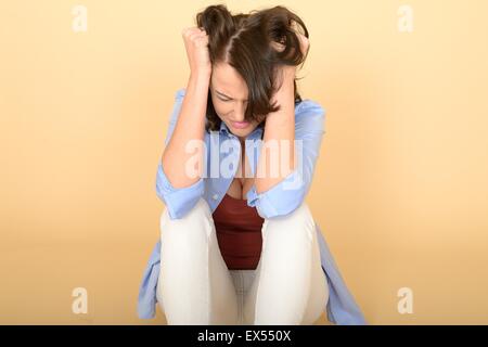 Attraktive schöne traurig deprimiert und wütend junge Frau sitzt auf dem Boden trug ein blaues Hemd und weiße Jeans Stockfoto