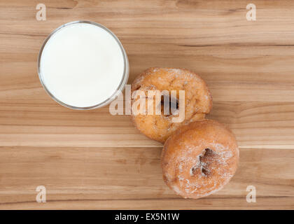 Zwei Krapfen und Glas Milch auf Holztisch Oberfläche. Stockfoto