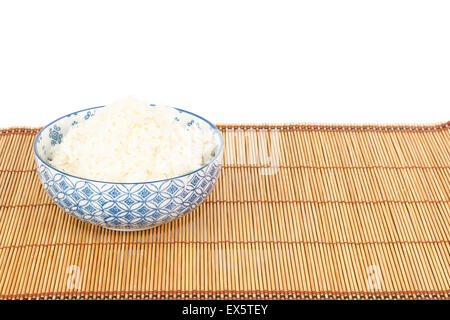 Schüssel mit Reis auf Tischset im asiatischen Stil vor weißem Hintergrund Stockfoto