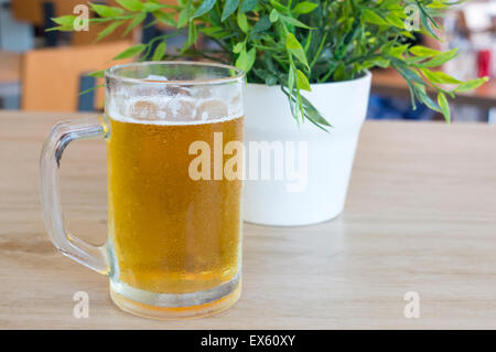 Bierkrug gefüllt mit frischem Bier vom Fass auf einem Tisch neben einer Pflanze Stockfoto