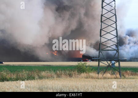 Rainham, London, UK. Dienstag, 7. Juli 2015. Über 80 Feuerwehrleute bekämpfen Brand in einer Palette Hof in Rainham. 12 Feuerwehrautos aus drei Feuerwehren wurden um ca. 20:00 Dienstag Abend in der Szene genannt. Kent und Essex, Feuerwehr und Rettungsdienste wurden gerufen, um die Londoner Feuerwehr unterstützen, bekämpfen das Feuer. Ein Stapel von Paletten und etliche Gebäude sind vermutlich in das Feuer. Form, die der Brand kilometerweit sehen konnte, wie Winde angefacht zu rauchen. Es gibt keine gemeldeten Verletzungen und die Ursache für den Brand ist noch nicht bekannt. Stockfoto