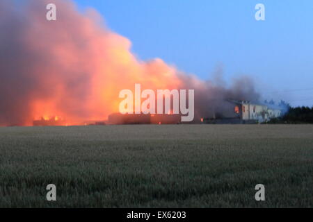 Rainham, London, UK. Dienstag, 7. Juli 2015. Über 80 Feuerwehrleute bekämpfen Brand in einer Palette Hof in Rainham. 12 Feuerwehrautos aus drei Feuerwehren wurden um ca. 20:00 Dienstag Abend in der Szene genannt. Kent und Essex, Feuerwehr und Rettungsdienste wurden gerufen, um die Londoner Feuerwehr unterstützen, bekämpfen das Feuer. Ein Stapel von Paletten und etliche Gebäude sind vermutlich in das Feuer. Form, die der Brand kilometerweit sehen konnte, wie Winde angefacht zu rauchen. Es gibt keine gemeldeten Verletzungen und die Ursache für den Brand ist noch nicht bekannt. Stockfoto