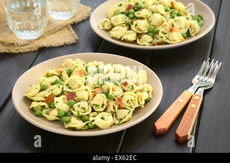 Tortellini-Salat mit grünen Erbsen, gebratenem Speck und Petersilie serviert auf Platten, mit Gabeln und Gläser Wasser auf der Seite Stockfoto