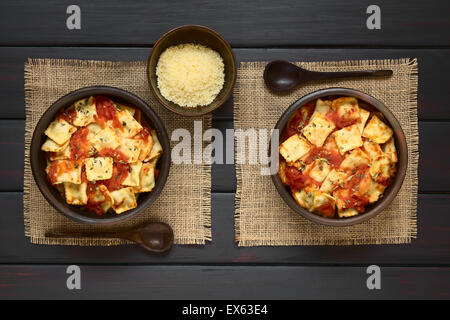 Gebackene Ravioli mit hausgemachter Tomatensauce in rustikale Schalen mit geriebenem Käse und Kochlöffel auf der Seite, über Kopf fotografiert Stockfoto