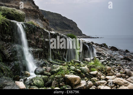 Landschaftsbild der Wasserfall fließt auf felsigen Strand bei Sonnenaufgang Stockfoto