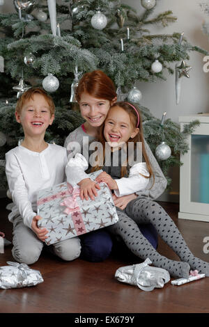 Heiligabend, glücklich Geschwister mit Weihnachtsgeschenke unter dem Weihnachtsbaum, Bayern, Deutschland Stockfoto