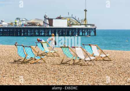 Traditionelle Old-fashioned, leer, blau und weiß gestreifte Liegestühle am Strand, mit Palace Pier, Brighton, East Sussex, UK Stockfoto