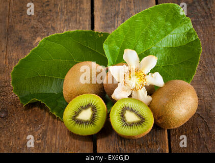 Reife Kiwis mit ihren Blättern und Blüten auf Holztisch Stockfoto