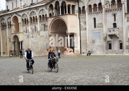 Zwei ältere Radfahrer fahren über Piazza Grande mit Modena Kathedrale im Hintergrund. Stockfoto