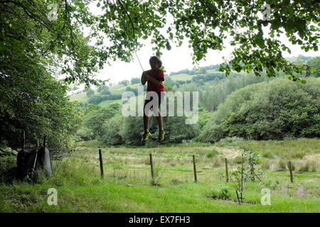 Jungen im Alter von 10 spielen im Freien auf einer Schaukel im ländlichen Garten mit Blick auf die Landschaft, Carmarthenshire, Wales UK KATHY DEWITT Stockfoto