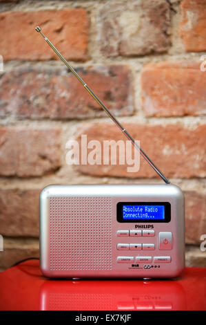 Kleine silberne Digitalradio abgestimmt auf Absolute Radio auf einen roten Tisch gegen einen rustikalen inneren Mauer Stockfoto
