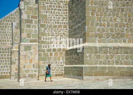 Frau mit gesenktem Kopf zu Fuß durch strukturierte Steinmauer der Kirche von Einsamkeit in Oaxaca, Mexiko Stockfoto