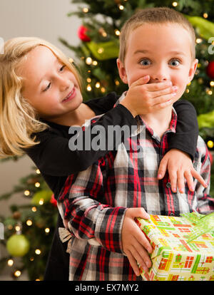 Schwester (6-7) Verkleidung Mund Bruders (6-7) mit der Hand während der Weihnachtsfeier Stockfoto