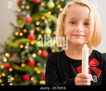 Mädchen (6-7) halten Kerze vor Weihnachtsbaum Stockfoto