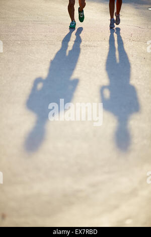 Zwei Beinpaare in Sport-Schuhe und Schatten des Paares auf Asphaltstraße Stockfoto