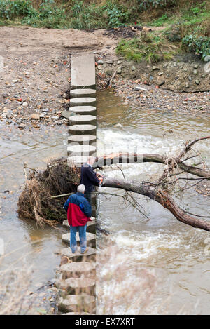 Zwei Männer stehen am Flüsschen Fußgängerbrücke Zerschneiden eines umgestürzten Baumes mit einer Kette sah England Stockfoto