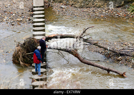 Zwei Männer stehen am Flüsschen Fußgängerbrücke Zerschneiden eines umgestürzten Baumes mit einer Kette sah England Stockfoto