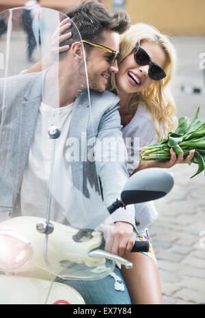 Entzückende Dame sitzt auf dem Roller mit ihrem Freund Stockfoto