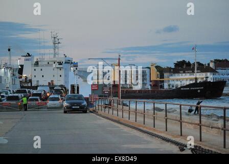 Autos, die auf der Purbeck-Seite die Sandbanks-Kettenfähre besteigen, wobei das Frachtschiff nach Poole Harbour, Dorset, Großbritannien, einfährt Stockfoto