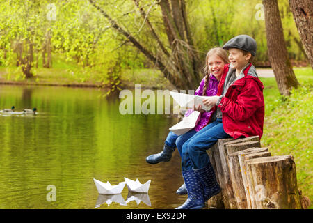 Lachende Mädchen und jungen in der Nähe von Teich mit Papierschiffchen Stockfoto