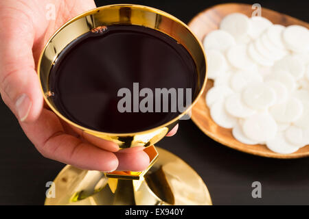 Christliche Heilige Kommunion, Mannes Hand halten gold Kelch mit Wein, Hostie auf Platte Stockfoto