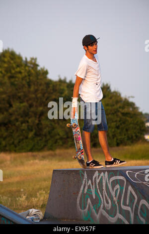 Skateboarder auf Rampe halten Skateboard in den späten Abend Sonne im Park Poole, Dorset im Juli Stockfoto