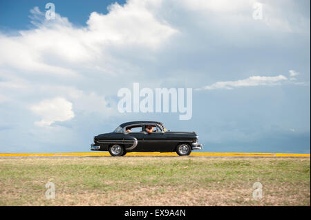 VARADERO, Kuba - 7. Juni 2011: Klassische amerikanische Oldtimer Laufwerke flach Küstenstraße gegen tropische Wolken. Stockfoto