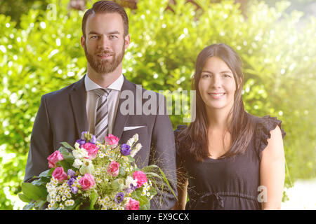 Glückliches junges Paar im Garten bei Bouquet von sortierte frische Blumen, lächelnd in die Kamera. Stockfoto