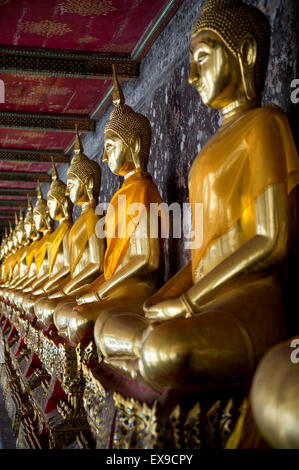 Reihe von Golden sitzenden Buddhas tragen gelbe Schärpe vor dekorative Wand in einem buddhistischen Tempel in Bangkok Thailand Stockfoto