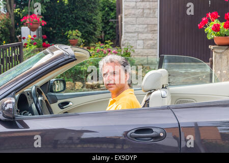 Seitenansicht des edlen senior Sportler mit drei-Tage-Bart und Salz Cand Pfeffer Haar trägt ein gelbes Poloshirt, während er dunkel braun in Wohngegend Autofahren ist Stockfoto